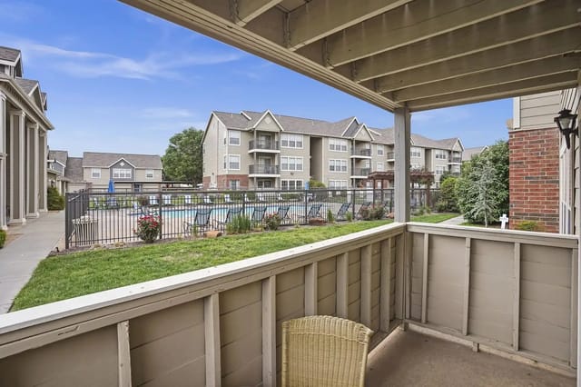 Balcony view of a community pool area with lounge chairs and apartment buildings in the background.