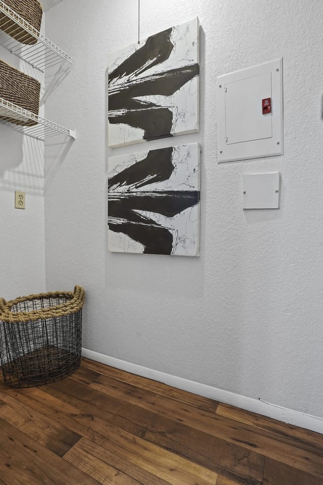 Narrow apartment storage nook with wood floor, abstract black-and-white wall art, and woven basket.