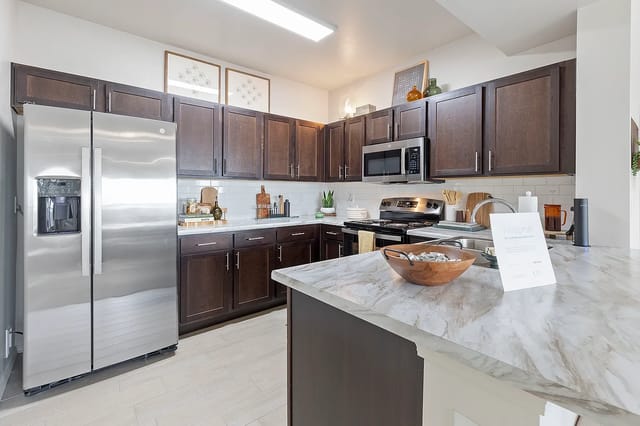 Modern kitchen in an apartment with dark wood cabinets, stainless steel appliances, and a marble island.