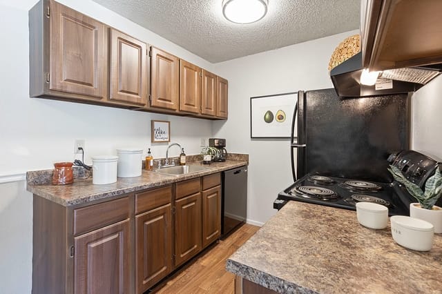 Kitchen in an apartment with wooden cabinets, brown countertops, sink, and a black stove.