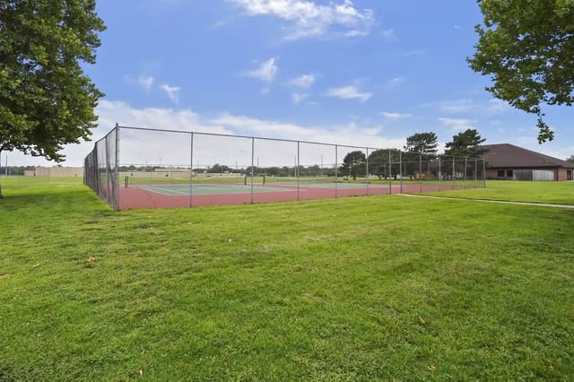 Fenced outdoor court with grassy foreground and a clubhouse in the background.
