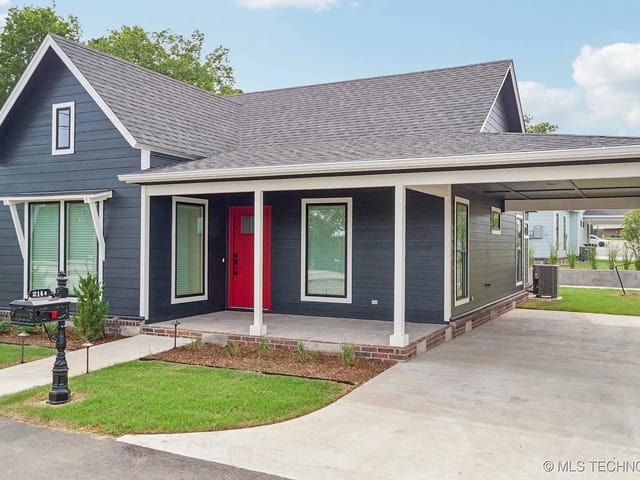 Exterior view of a black house with a red front door and a landscaped yard.