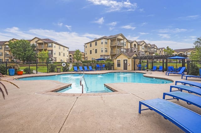 A swimming pool surrounded by blue lounge chairs and apartment buildings.
