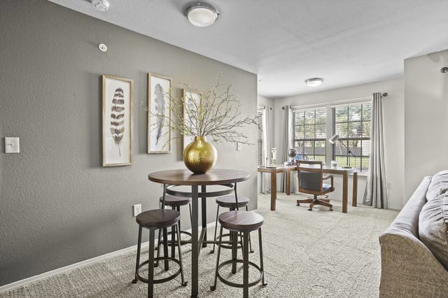 A round table with four stools and a vase of branches on it, with a desk and chair in the background.