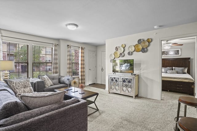 Living room with a sofa, coffee table, and TV, leading into a bedroom.