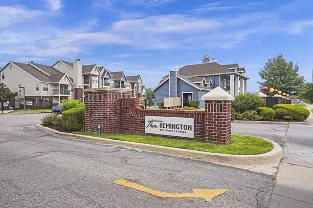 Brick entrance sign for The Remington apartment homes with blue buildings in the background.
