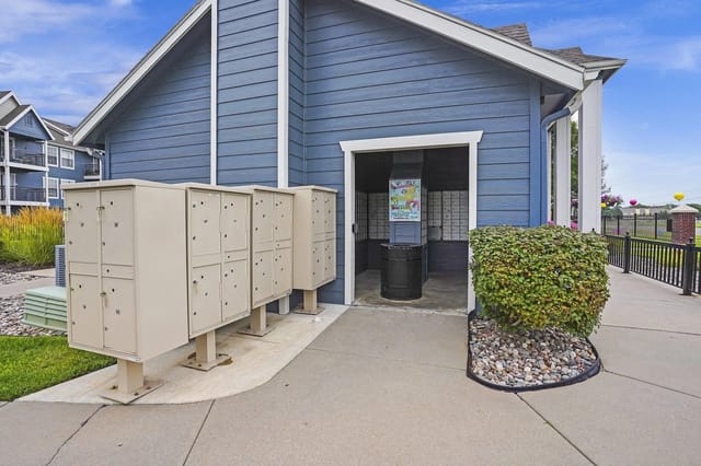 Exterior of blue apartment building with beige mailboxes and a hedge.