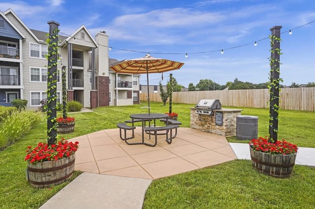 Outdoor community courtyard with a round picnic table, umbrella, grill, and string lights.