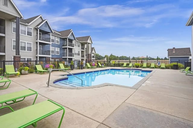 Outdoor pool at a multifamily community with lime-green lounge chairs and apartment buildings in the background.