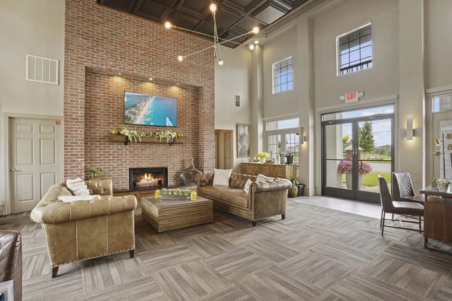 Spacious lobby with a brick fireplace, modern chandelier, and tan leather seating.