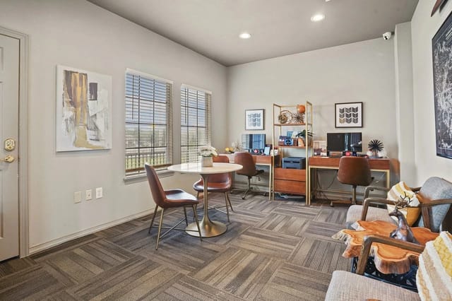 Interior resident lounge with round table, desks, chairs, and large windows.