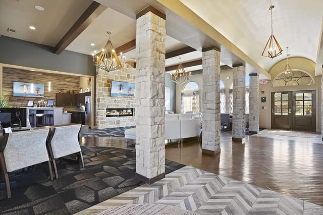 Community lounge area with stone-clad columns, a fireplace, seating, and a reception desk.