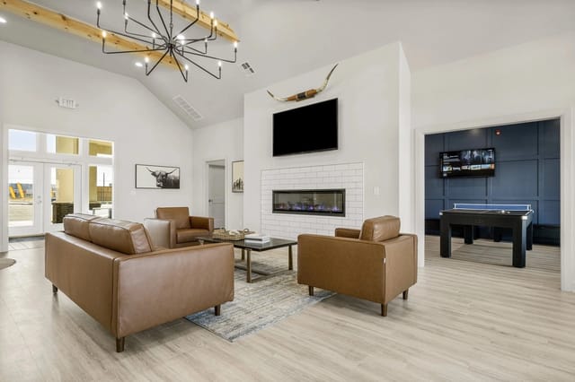 Modern communal lounge with brown leather seating, fireplace, TV, and foosball table.