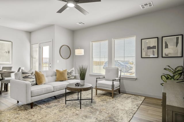 Bright apartment living room with a white sofa, armchair, rug, and large windows.