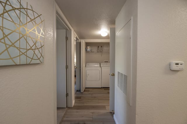 Hallway view into a laundry closet with a washer and dryer against the back wall.