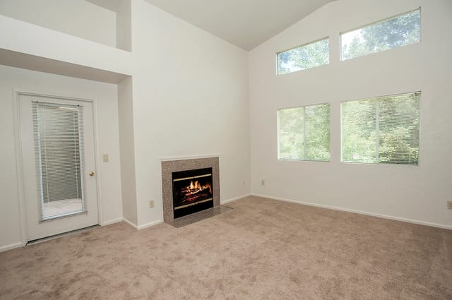 Living room with a fireplace, beige carpet, tall windows, and a glass door with blinds.