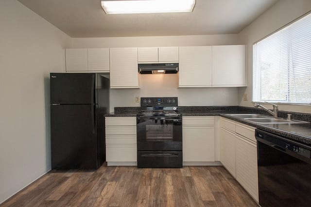 Kitchen in apartment with white cabinets, black appliances, and a large window.