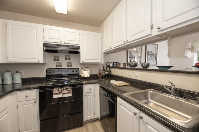 Kitchen area with white cabinets, black appliances, and a stainless steel sink.