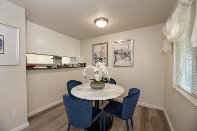 Dining area with a marble table and blue chairs, overlooking a kitchen pass-through.