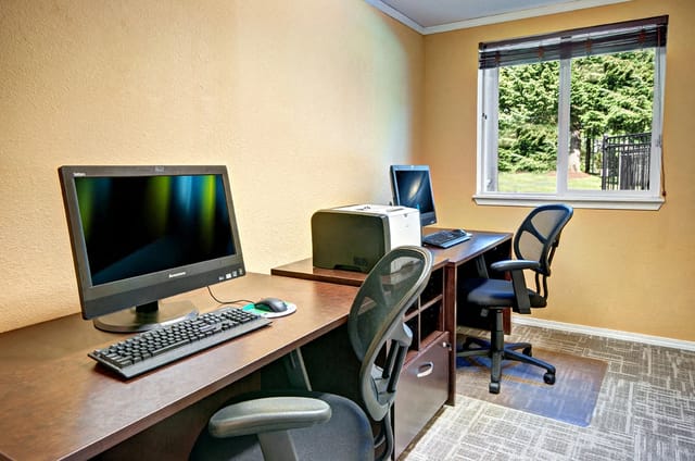 Bright apartment home office with two desks, chairs, computers, and a window view.