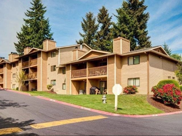 Exterior view of a beige apartment complex with balconies, green lawns, and a curved driveway.