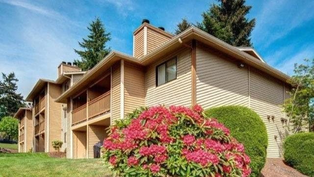 Exterior view of a tan multi-unit apartment building with balconies and landscaped shrubs.