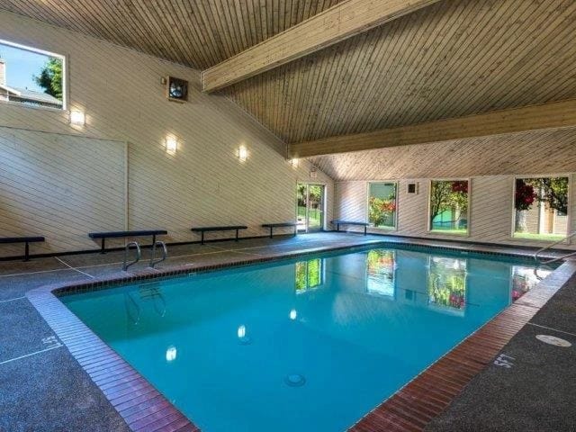 Indoor community pool area with wooden ceiling, benches, and large windows.