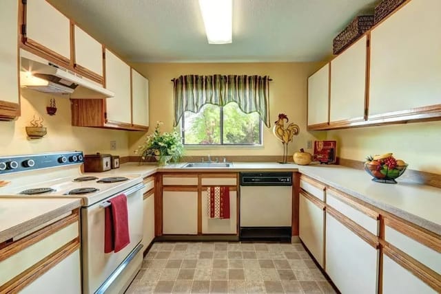U-shaped kitchen with white appliances and wood-tone cabinets, window over sink.