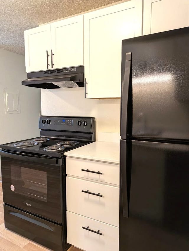 Kitchen featuring a black stove, white cabinets, and a black refrigerator.