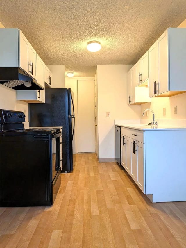 Modern kitchen with white cabinets, black appliances, and wood floors.