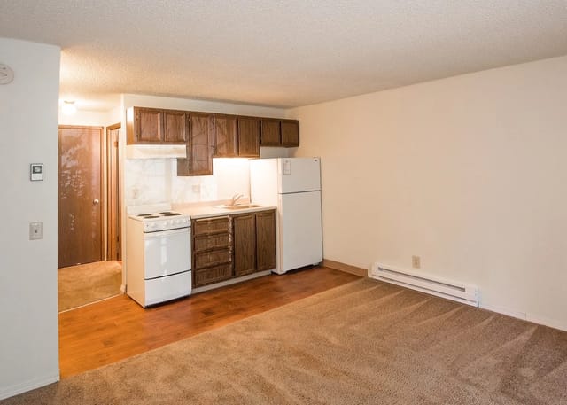 Kitchen with dark wood cabinets, white refrigerator and stove, and a small living area.