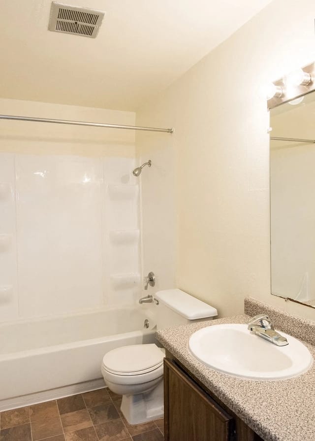 Bathroom in an apartment with a tub/shower, toilet, and speckled countertop vanity.