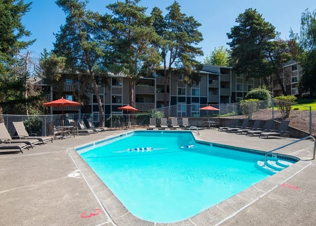 Outdoor apartment pool with lounge chairs and red umbrellas.