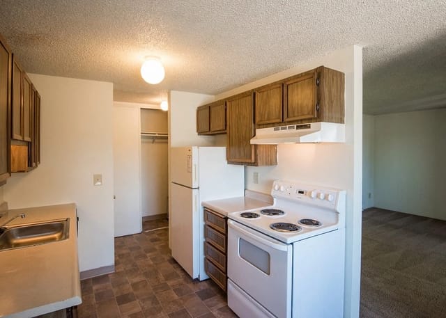 Kitchen in an apartment with wooden cabinets, white appliances, and tile flooring.