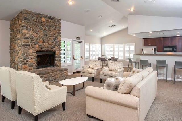 Community lounge area with a stone fireplace, comfortable seating, and a full-service kitchen.