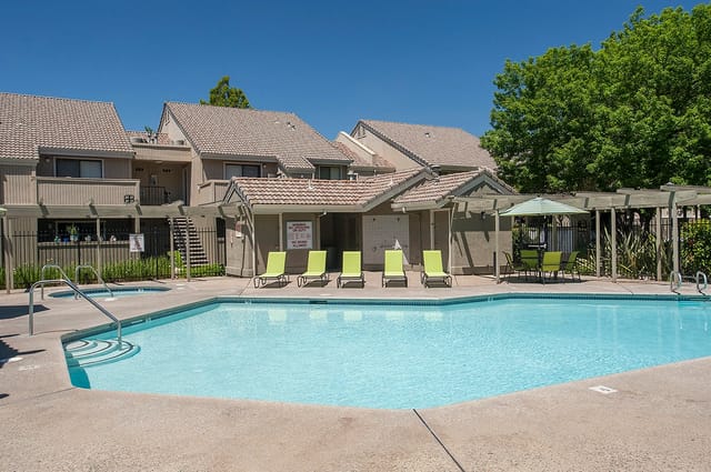 Outdoor apartment community pool with lounge chairs and a shaded seating area.