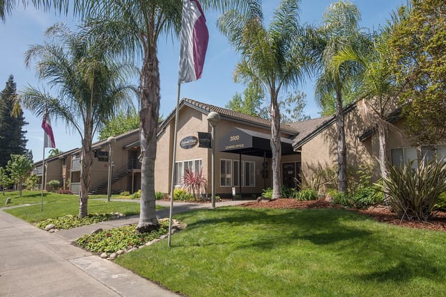 Building exterior of apartment complex with palm trees and leasing office sign.