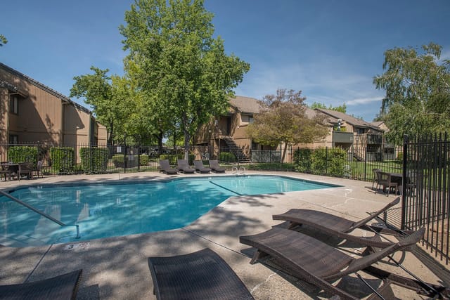 Outdoor apartment community pool with lounge chairs and a black metal fence.