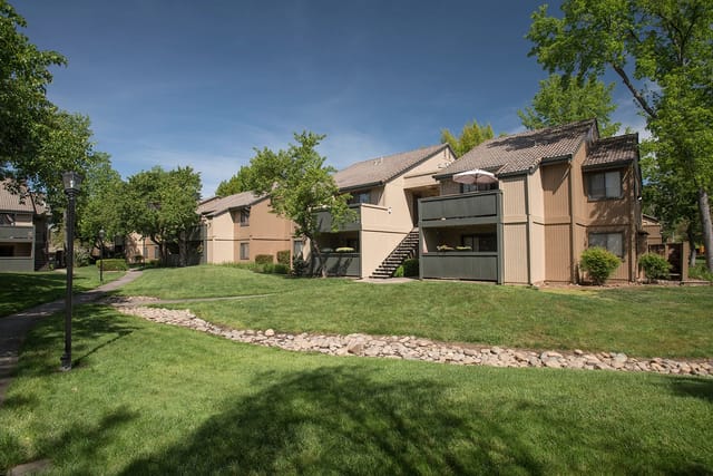 Exterior view of apartment buildings with green lawns and mature trees.
