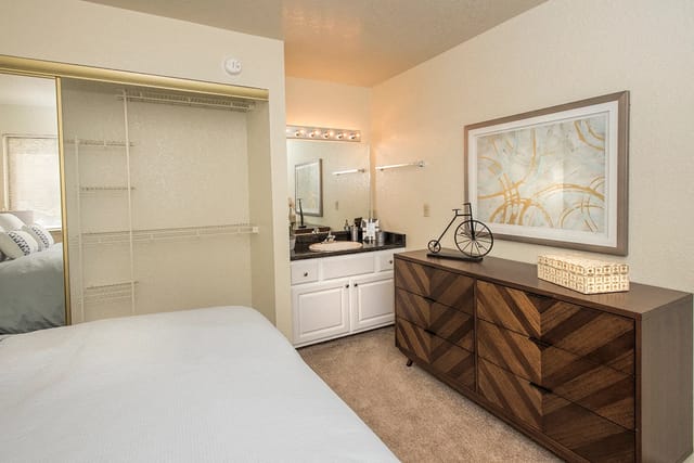 Bedroom in apartment with mirrored sliding closet, vanity, and a wooden dresser.