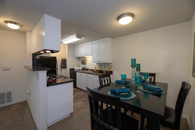 Kitchen and dining area in an apartment with white cabinets and a black dining table.