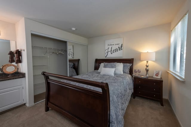 Bedroom with a dark wood bed, nightstand, closet, and window blinds.