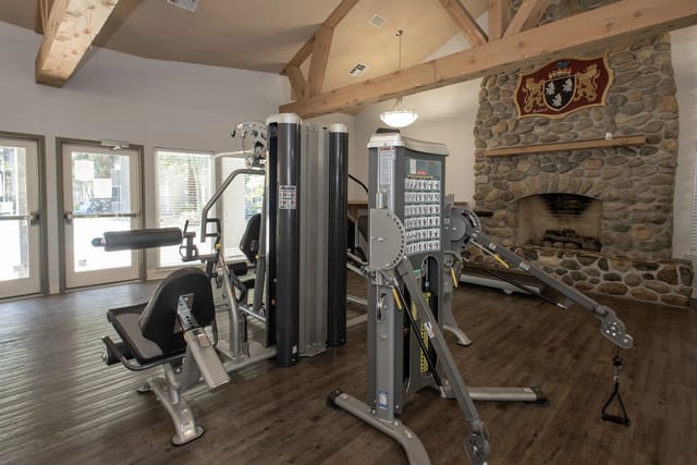 Indoor gym in clubhouse with weight machines and stone fireplace.