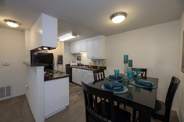 Kitchen and dining area in an apartment with white cabinets and a black dining table.