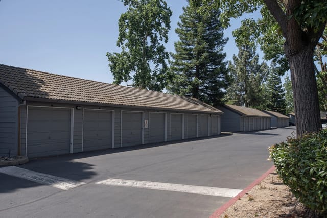 Row of gray garage doors along a paved driveway with trees behind.