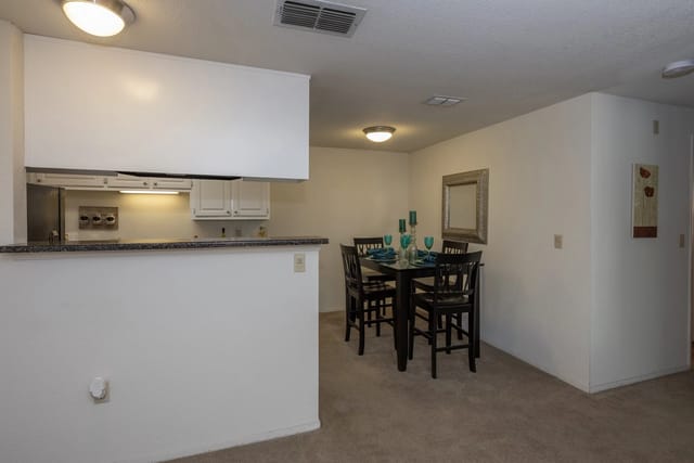 Open-concept kitchen and dining area with white cabinets, granite counter, and a dark wood table with chairs.