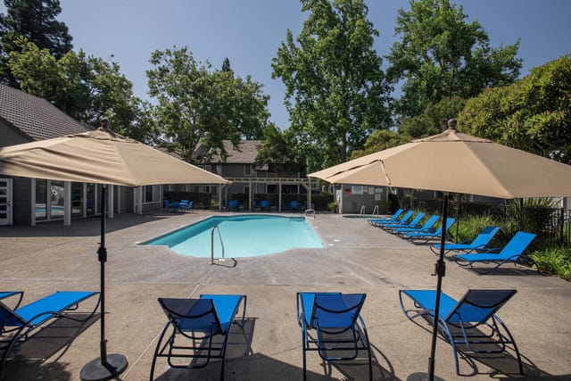 Apartment complex swimming pool with lounge chairs and umbrellas.