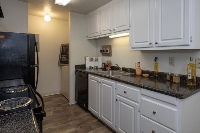 Kitchen with black refrigerator, white cabinets, granite countertops, and stainless steel sink.