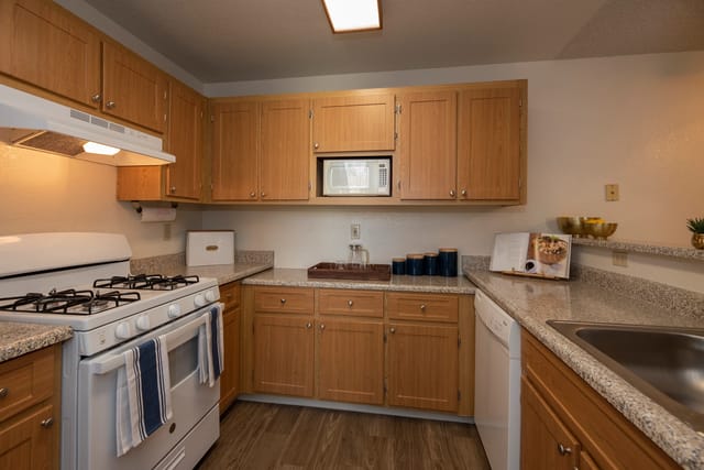 Kitchen in an apartment with wood cabinets, white stove, microwave, and sink.