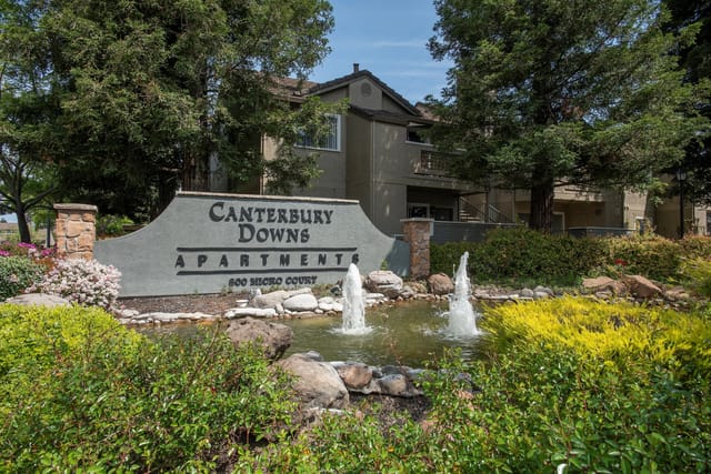 Exterior sign for Canterbury Downs Apartments with fountain and landscaping.